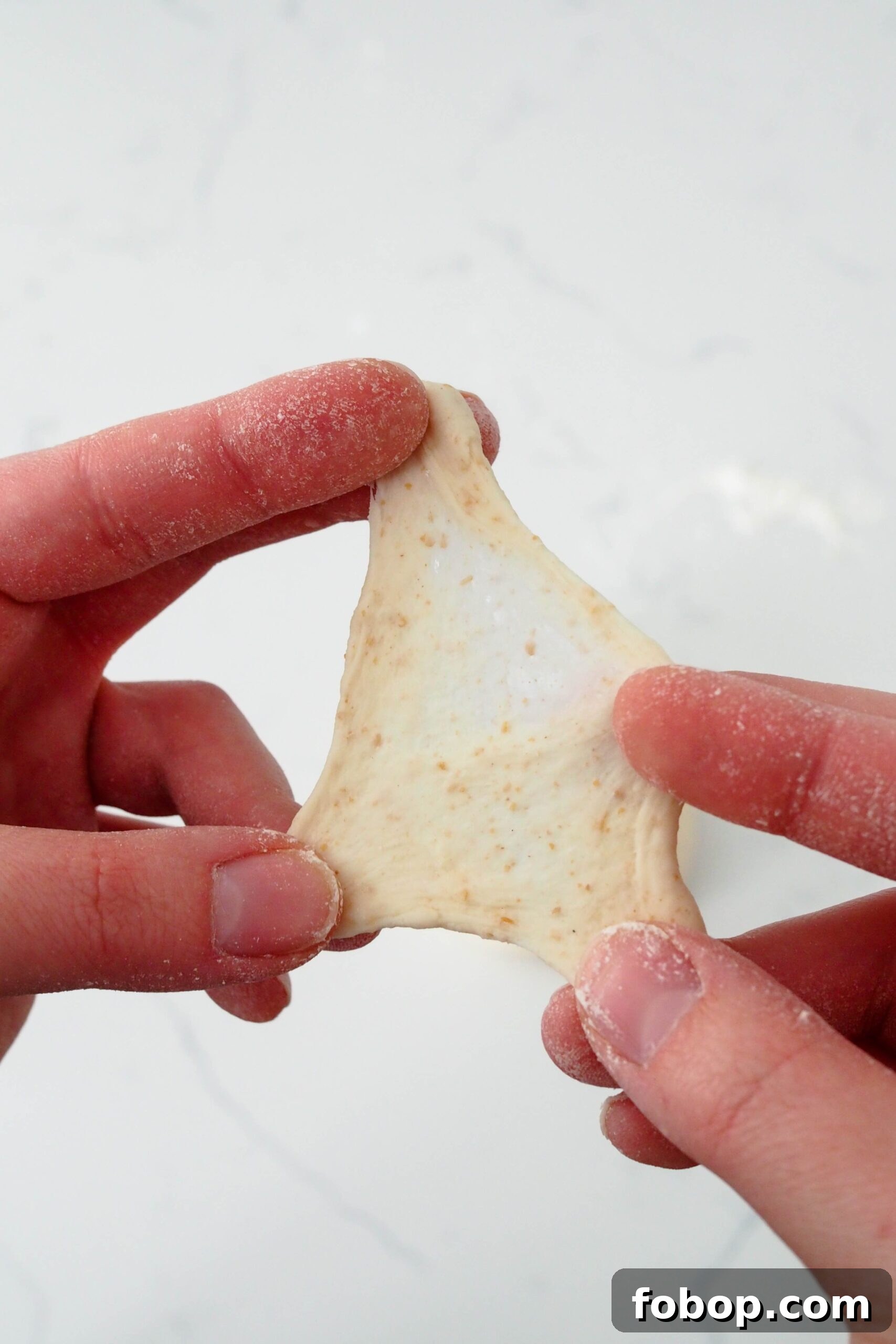 Two hands pull apart dough, revealing a stretchy, glutinous interior.
