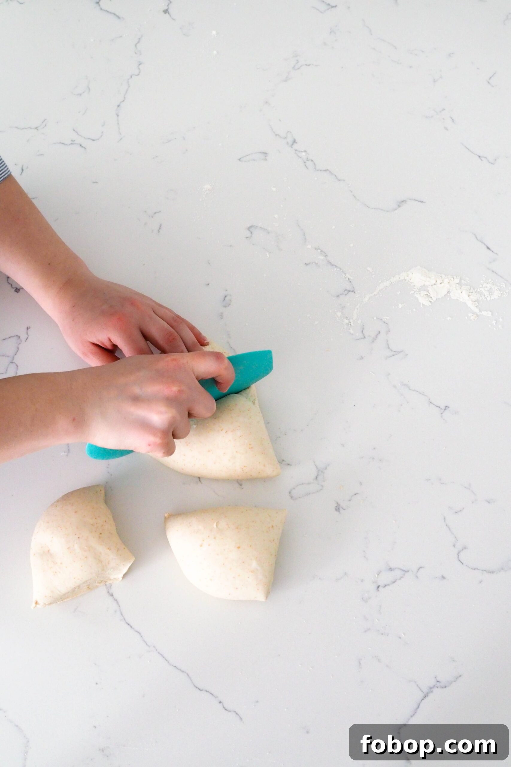 Two hands divide a ball of dough into four on a quartz counter.