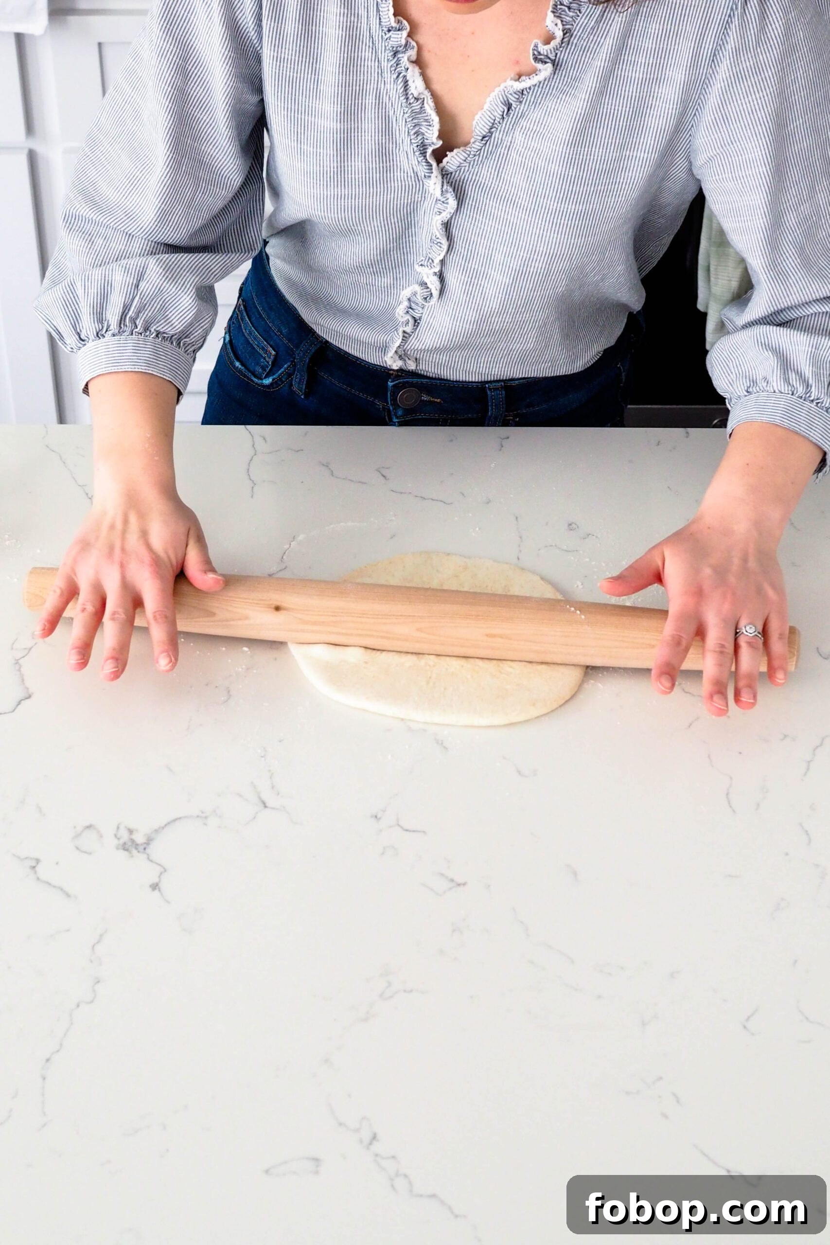 Two hands roll out a round of thin crust pizza dough.