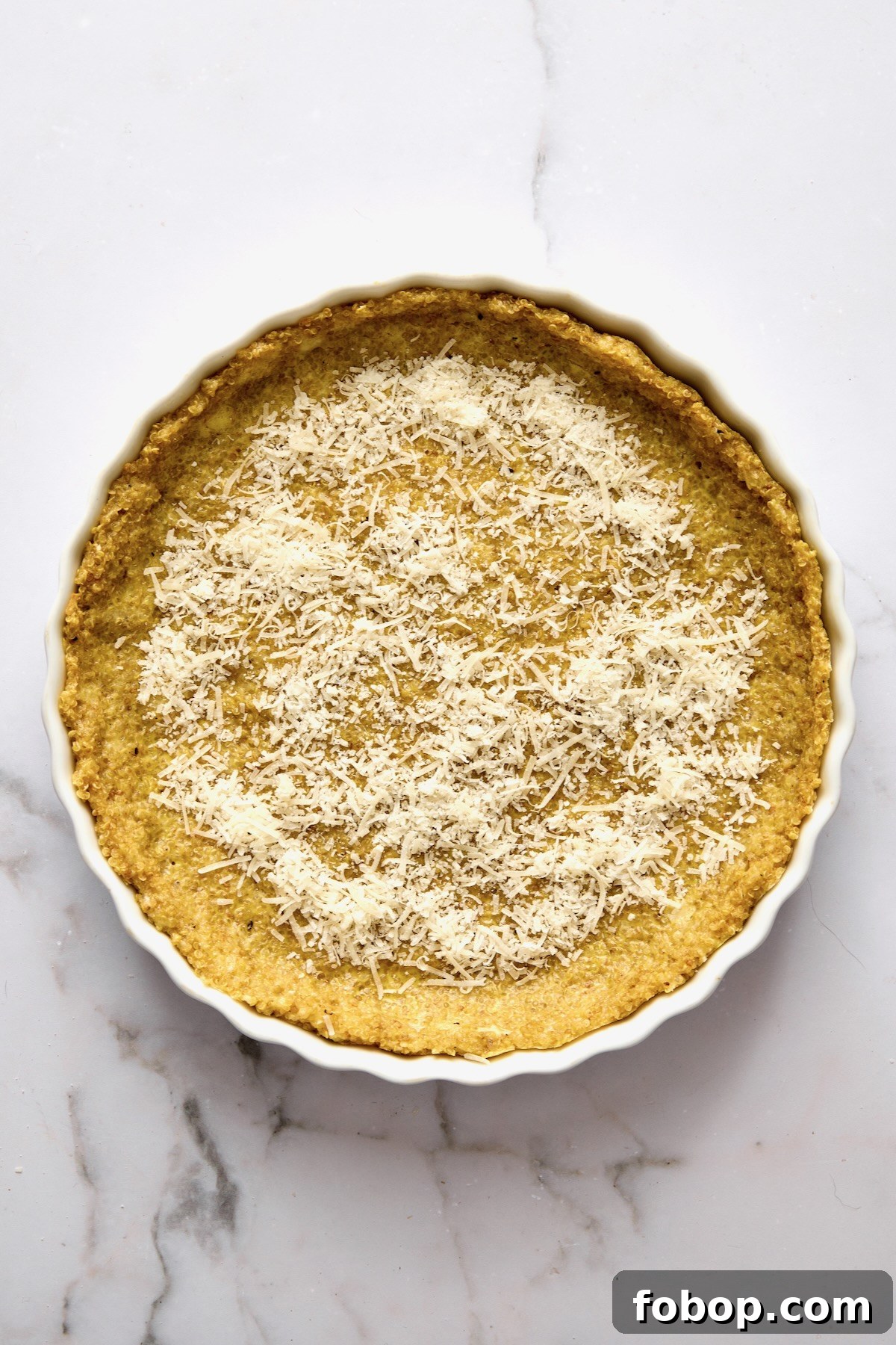 Baked quinoa crust in round white baking dish with Parmesan cheese sprinkled over the top.