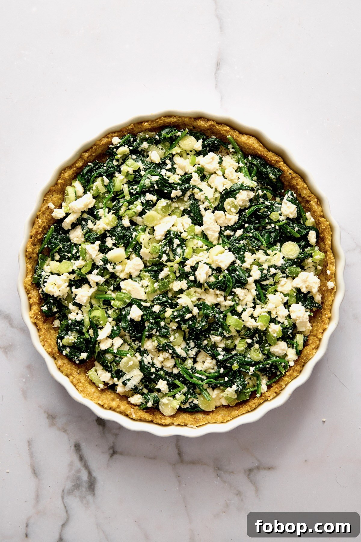 Spinach, scallion and feta cheese in baked quinoa crust in round white baking dish.