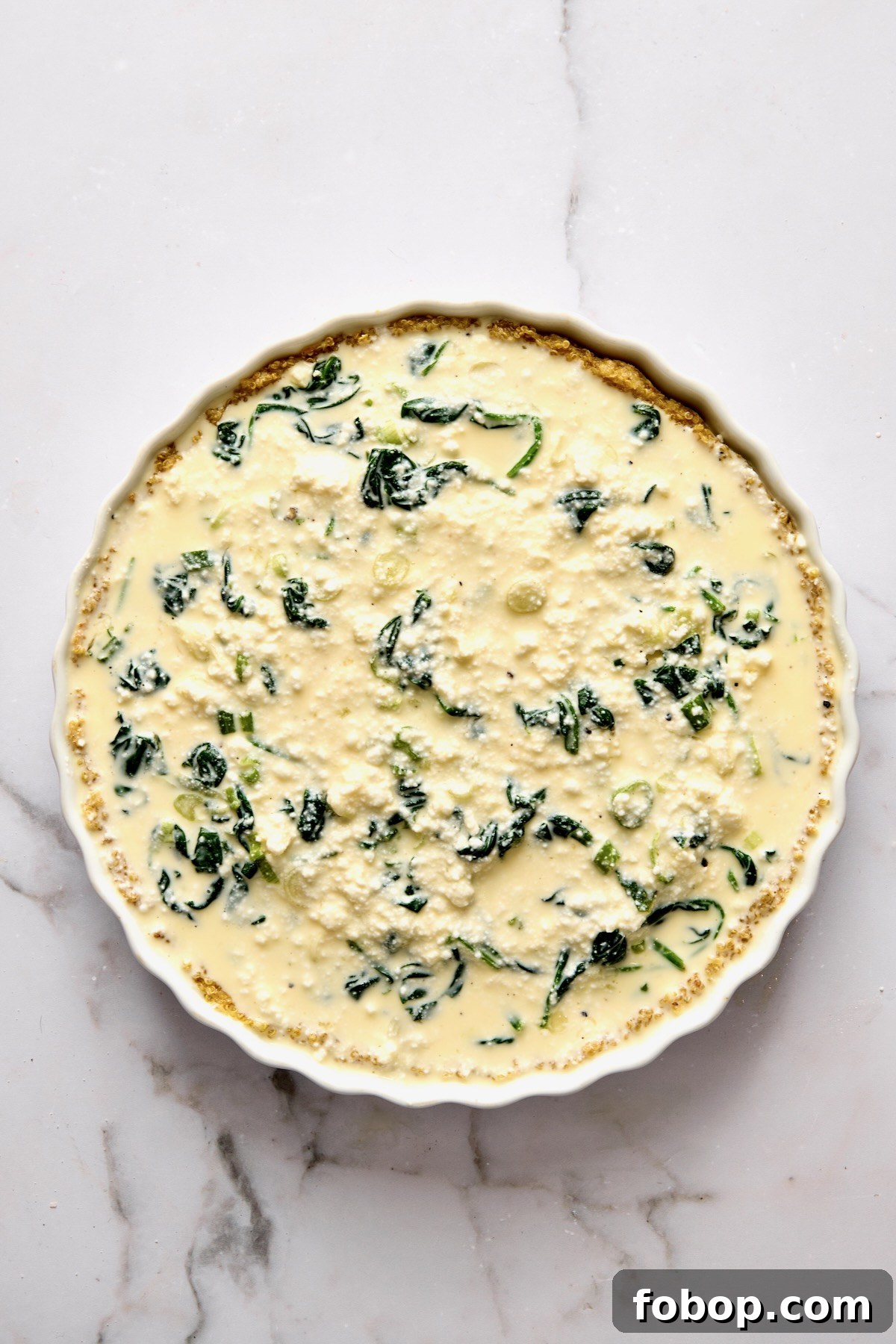 Custard for quiche poured over the other ingredients in round white baking dish.