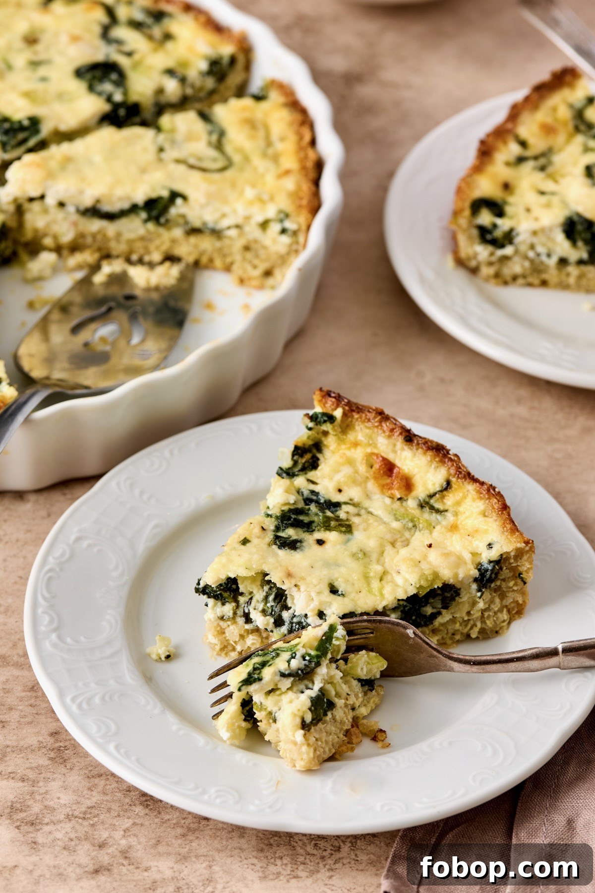 One piece of Spinach Feta Quiche with Quinoa Crust on white plate with fork cutting into it.