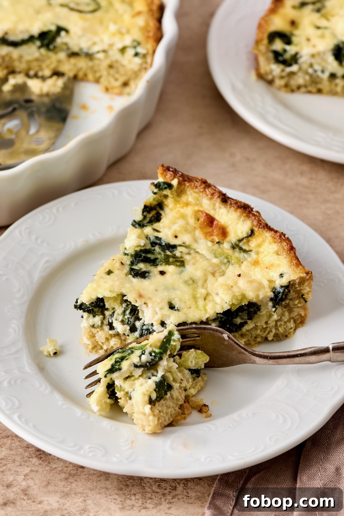 One piece of Spinach Feta Quiche with Quinoa Crust on white plate with fork cutting into it.