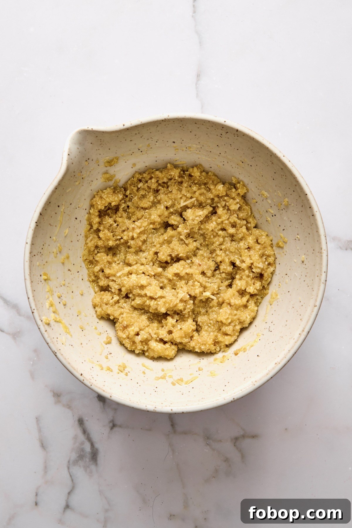 Cooked quinoa, eggs, and cheese combined in mixing bowl.