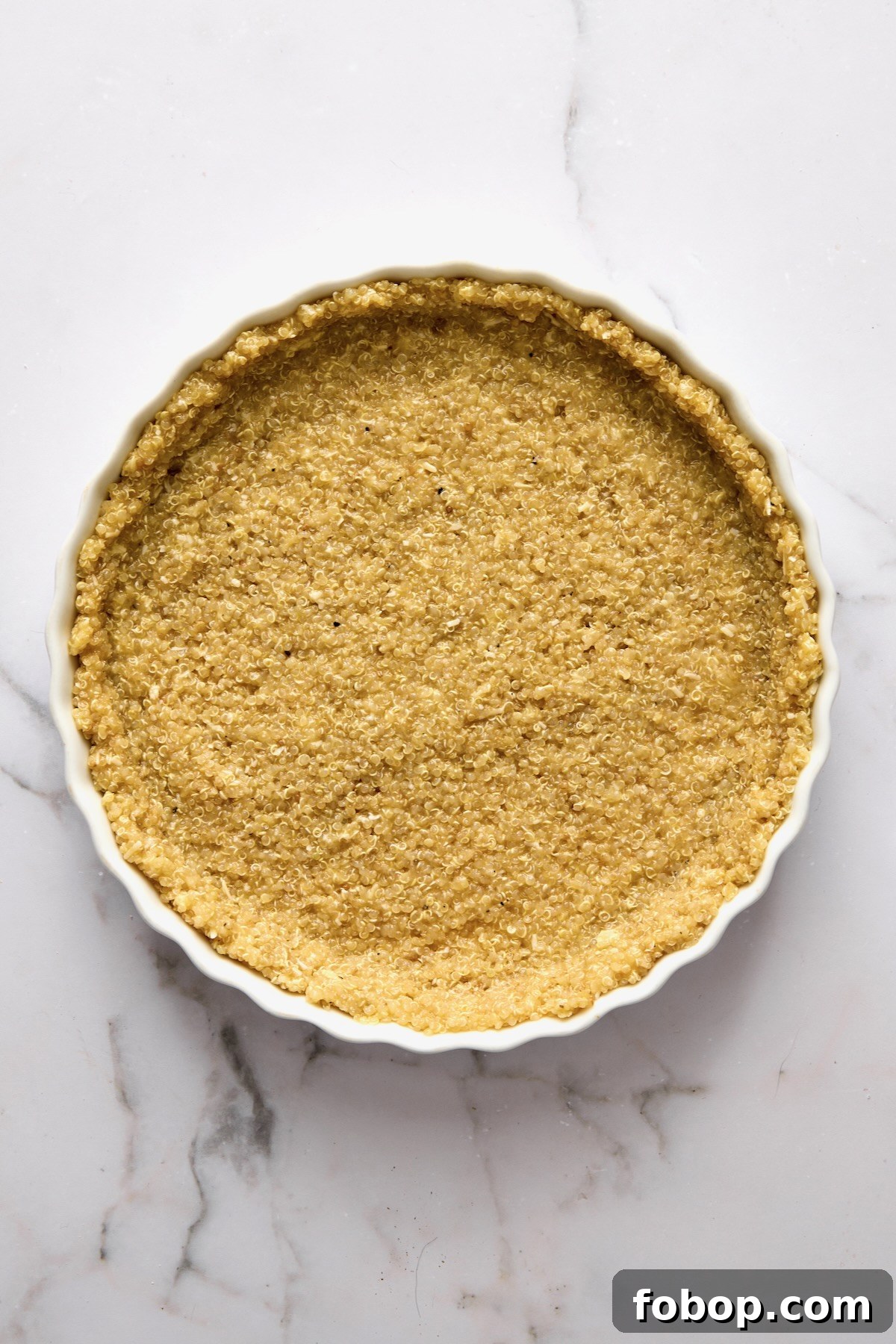 Unbaked quinoa crust in round white baking dish.