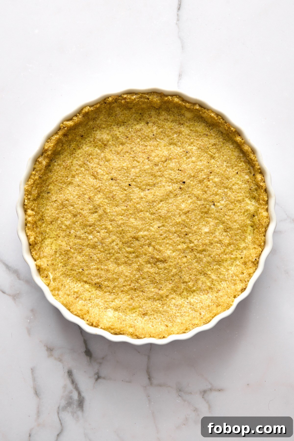 Baked quinoa crust in round white baking dish.