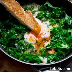 Creamy Scrambled Eggs with Sautéed Kale Breakfast Bowl 12 A toast soldier being dipped into a runny egg yolk in a pan of egg and cheesy kale
