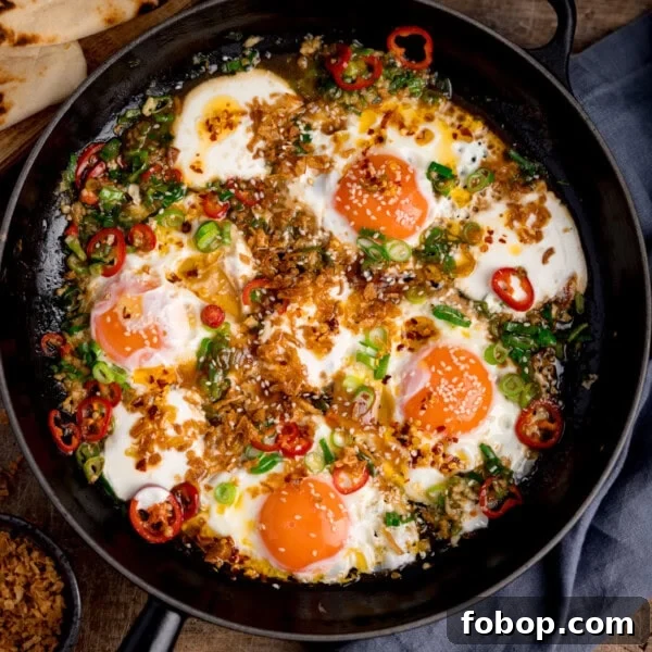 Creamy Scrambled Eggs with Sautéed Kale Breakfast Bowl 6 Square image of four sunny-side-up fried eggs in a skillet, topped with natural yogurt, fried onions, sliced red chiles, scallions, and sesame seeds.