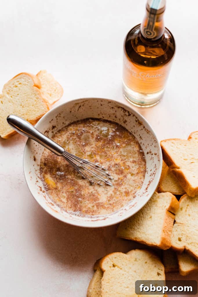 A bowl of french toast batter on a light pink surface, with slices of brioche scattered around