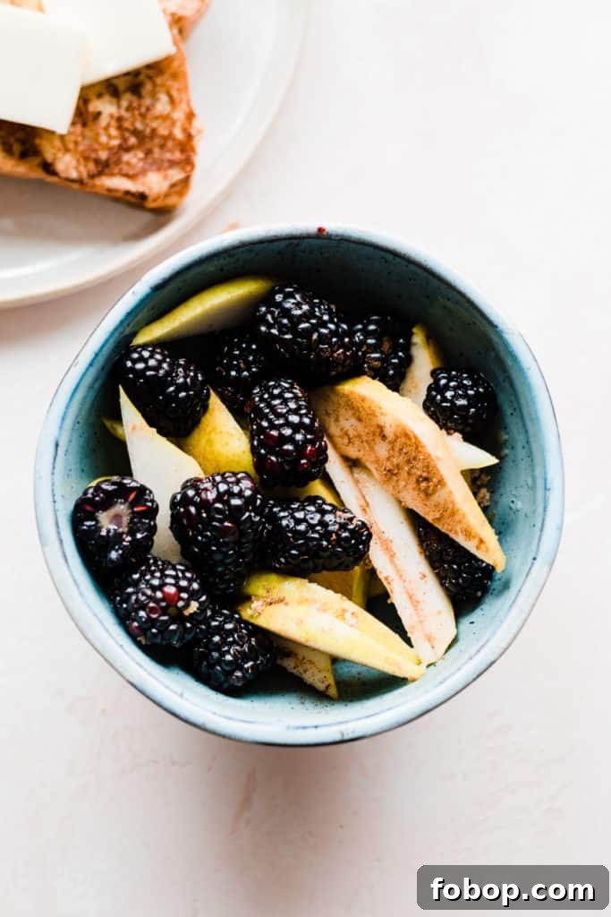 A blue bowl of blackberries and pear slices sprinkled with cinnamon, brown sugar, and rum