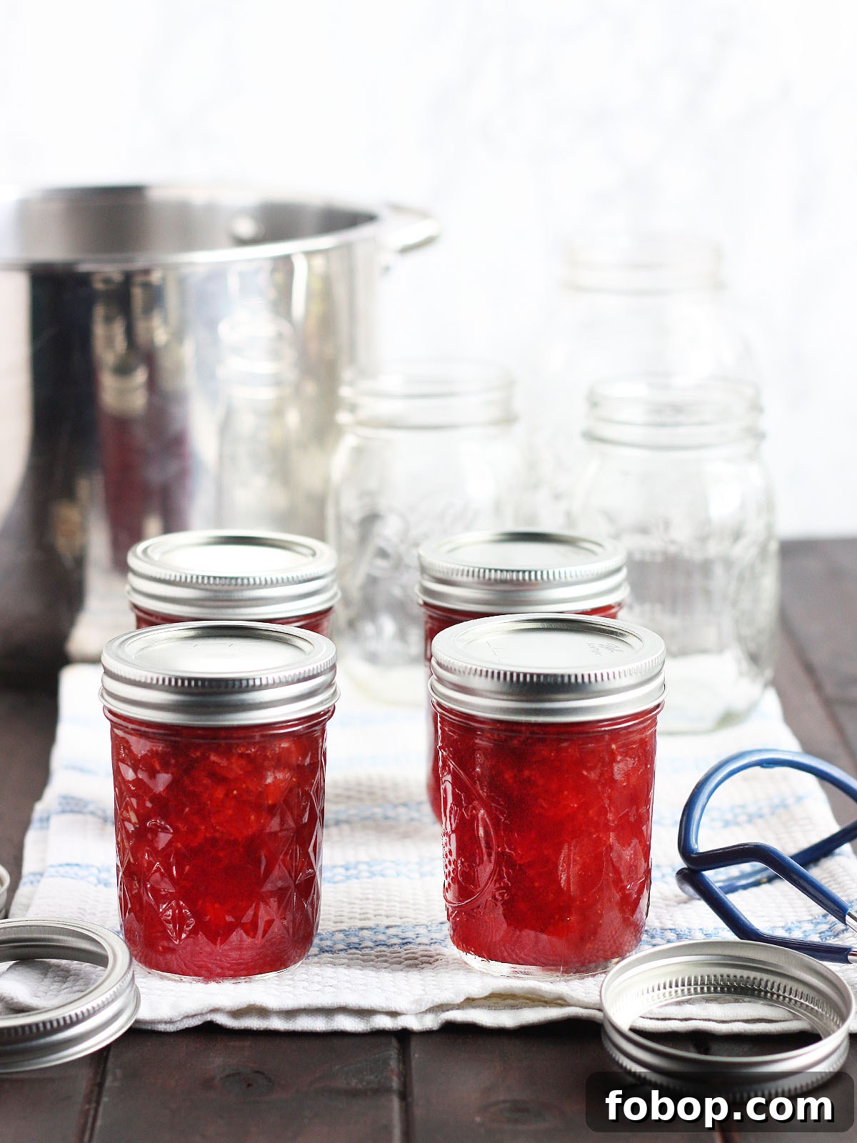 four jars of homemade jam cooling on a towel with empty mason jars and canning rings in the background