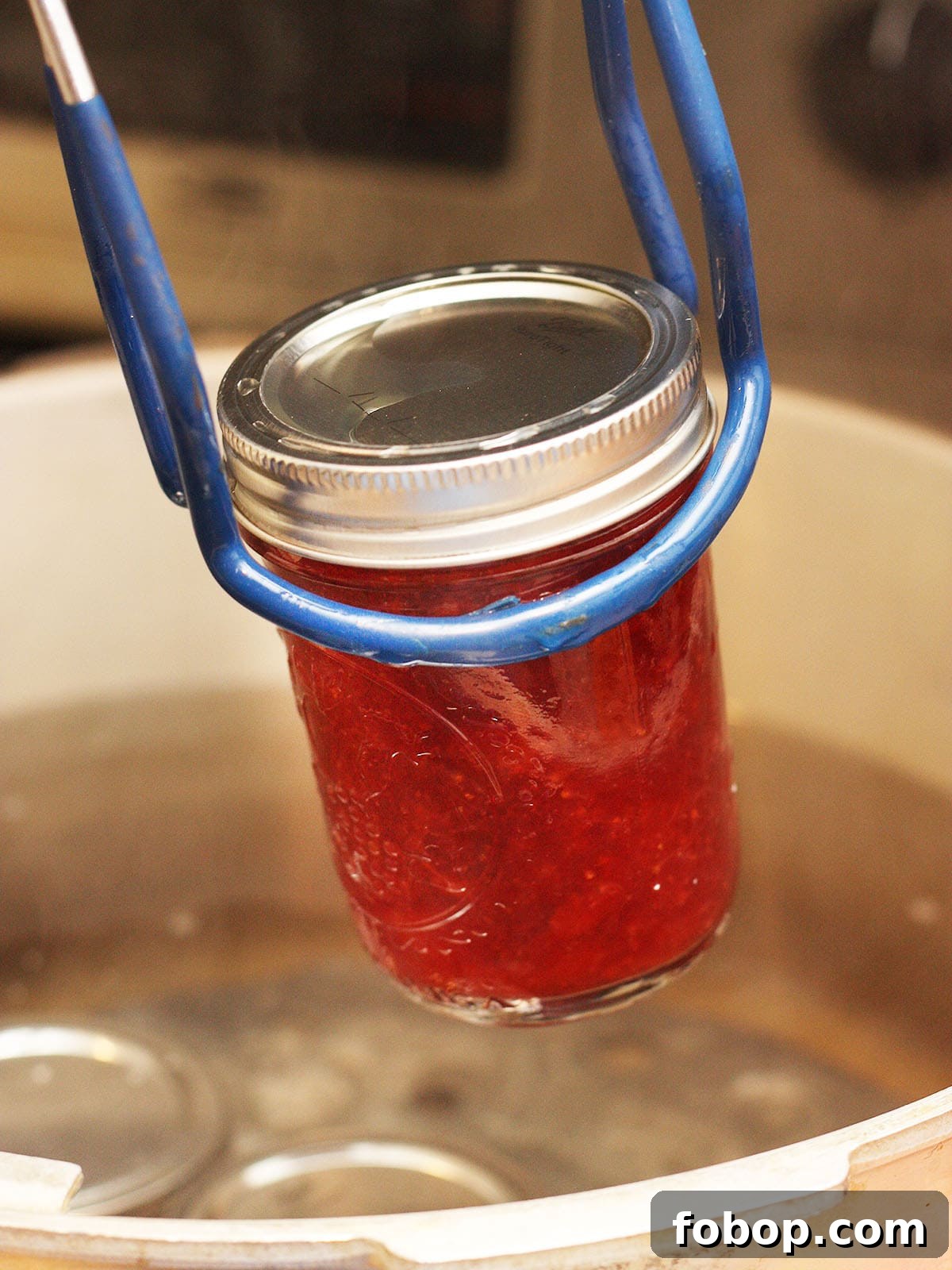 using a jar lifter to remove a jar of jam from a stock pot after water bath canning