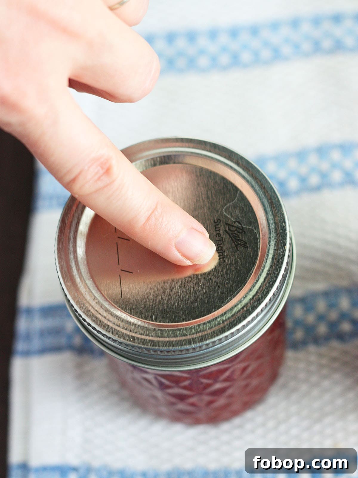 finger pressing down on the center of a lid to check for a seal