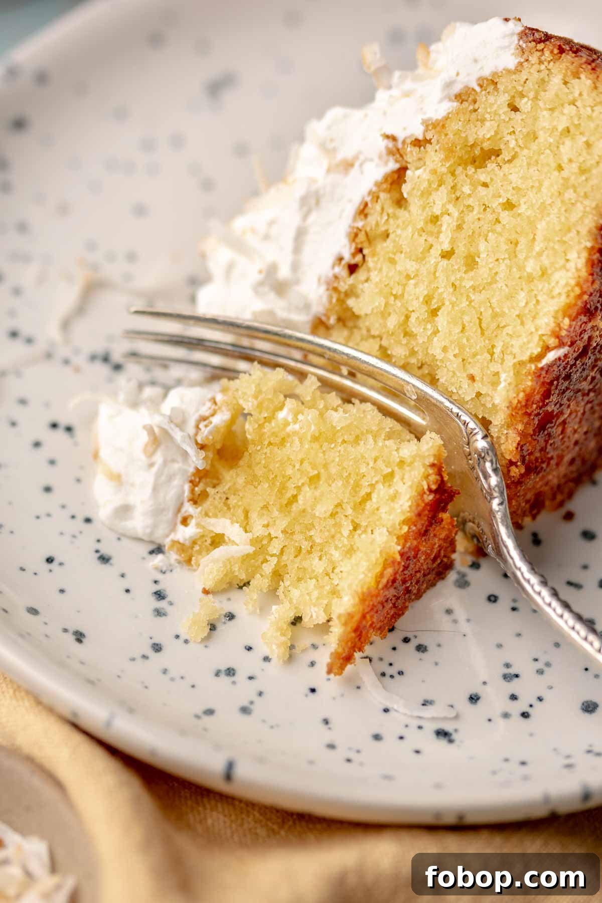 Coconut Almond Cake Recipe with Moist Layers and Toasted Almonds 2 A fork cuts through a piece of coconut cake on a plate.
