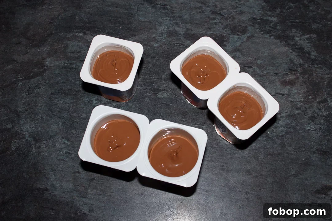Melted milk chocolate in small yoghurt pots with wooden teaspoons pressed in the middle