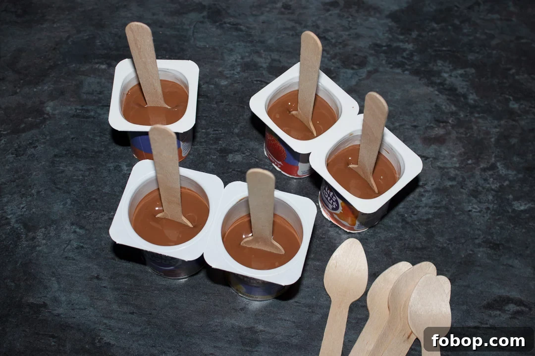 Melted milk chocolate in small yoghurt pots with wooden teaspoons pressed in the middle