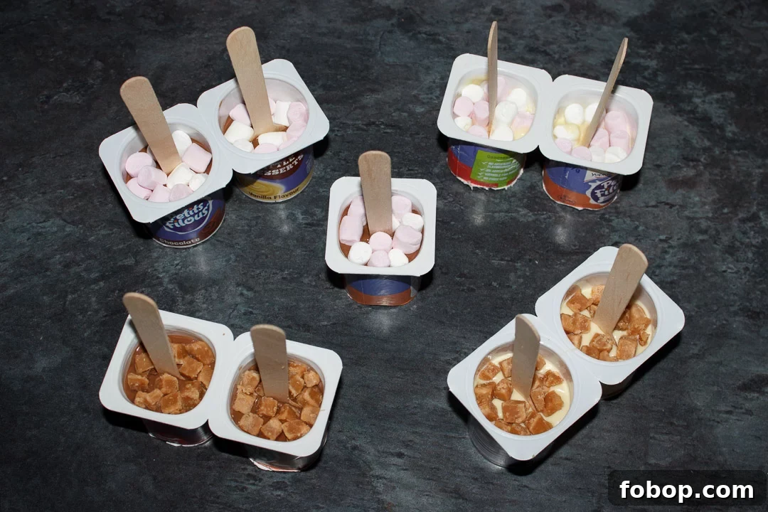 Hot chocolate sticks topped with mini marshmallows and fudge pieces, ready to be put in the fridge to set