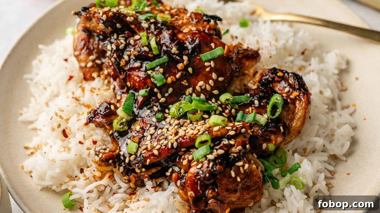 A plate of white rice topped with glazed chicken pieces, garnished with sesame seeds and chopped green onions.