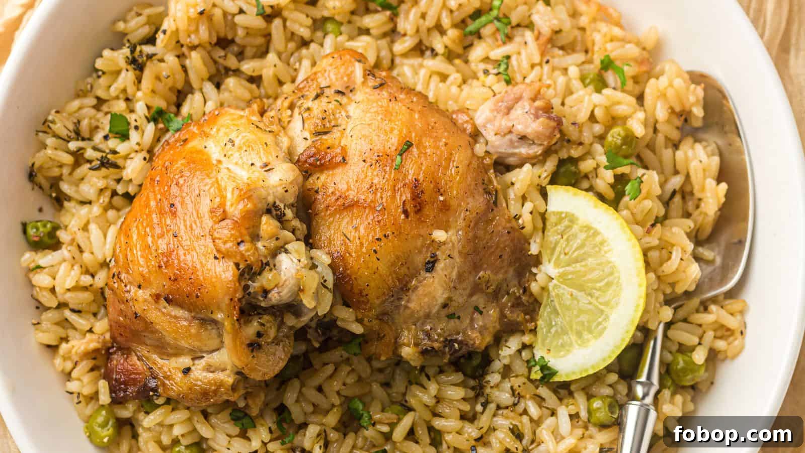 A plate of seasoned rice with green peas, topped with two pieces of roasted chicken and a lemon slice, served with a spoon.