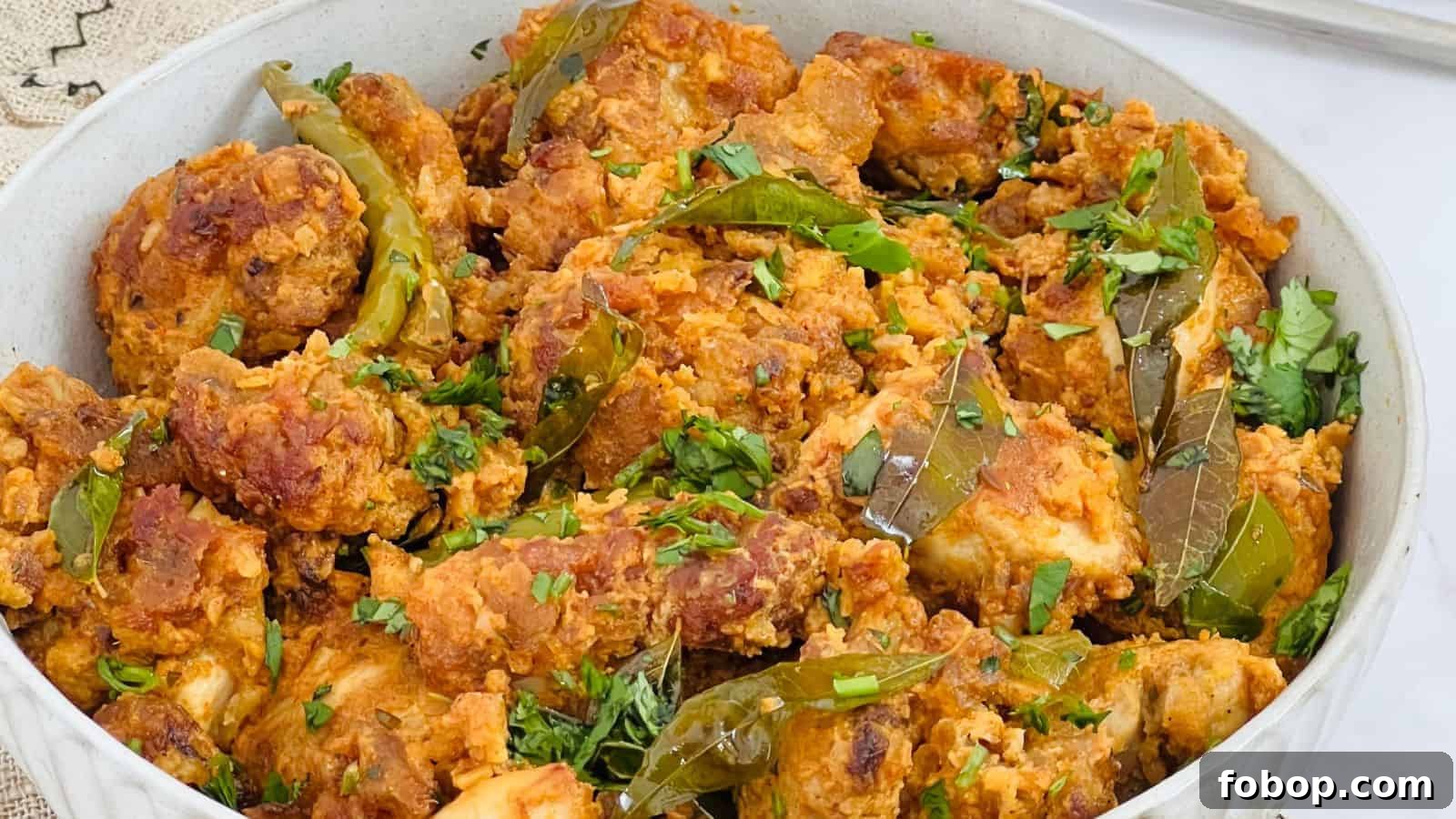 A dish of Chicken 65 seasoned with herbs and spices, garnished with chopped cilantro and green chili peppers in a white bowl.