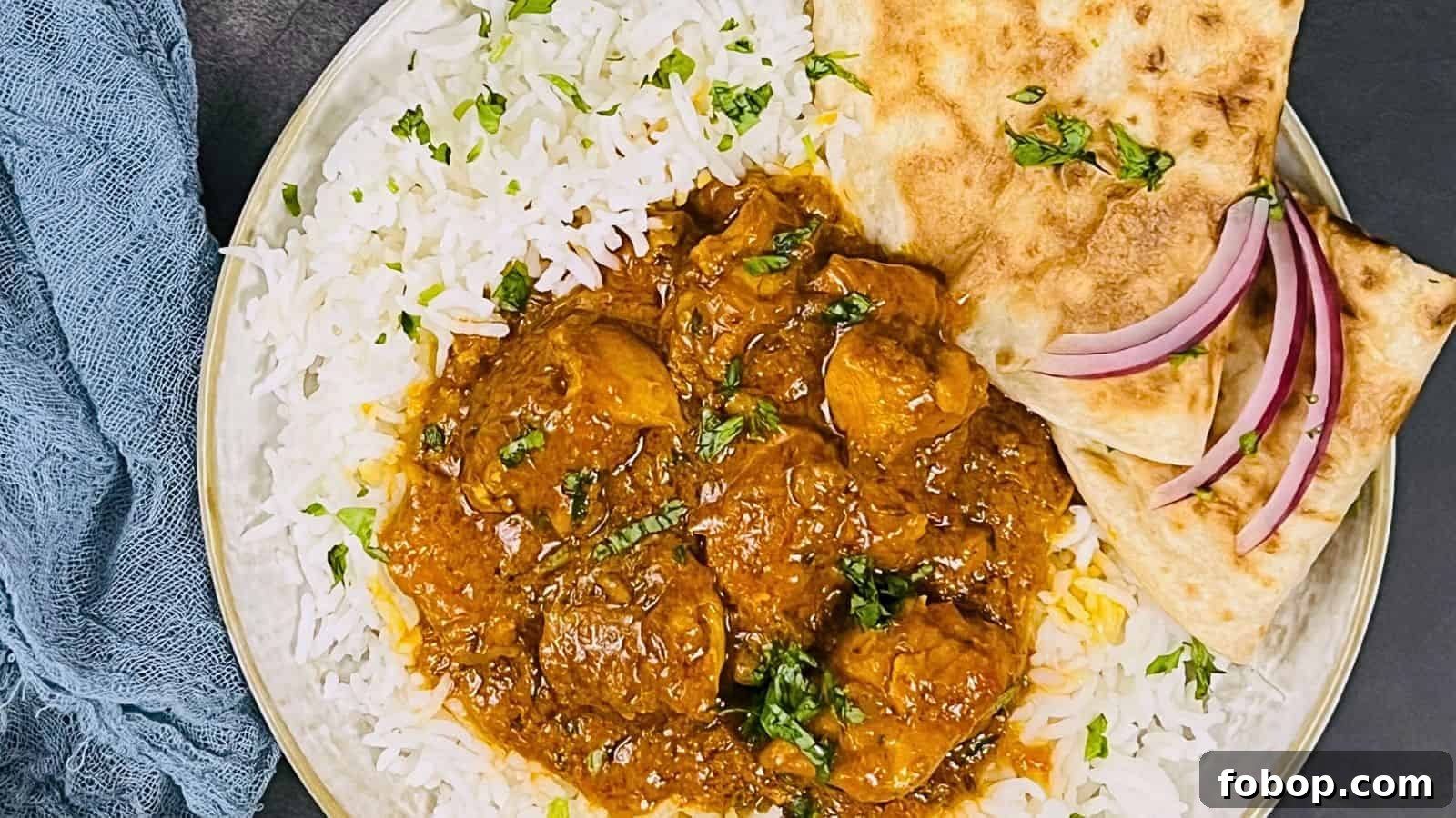 A plate of Chicken Masala with two pieces of naan and basmati rice garnished with herbs, served with sliced onions on the side.