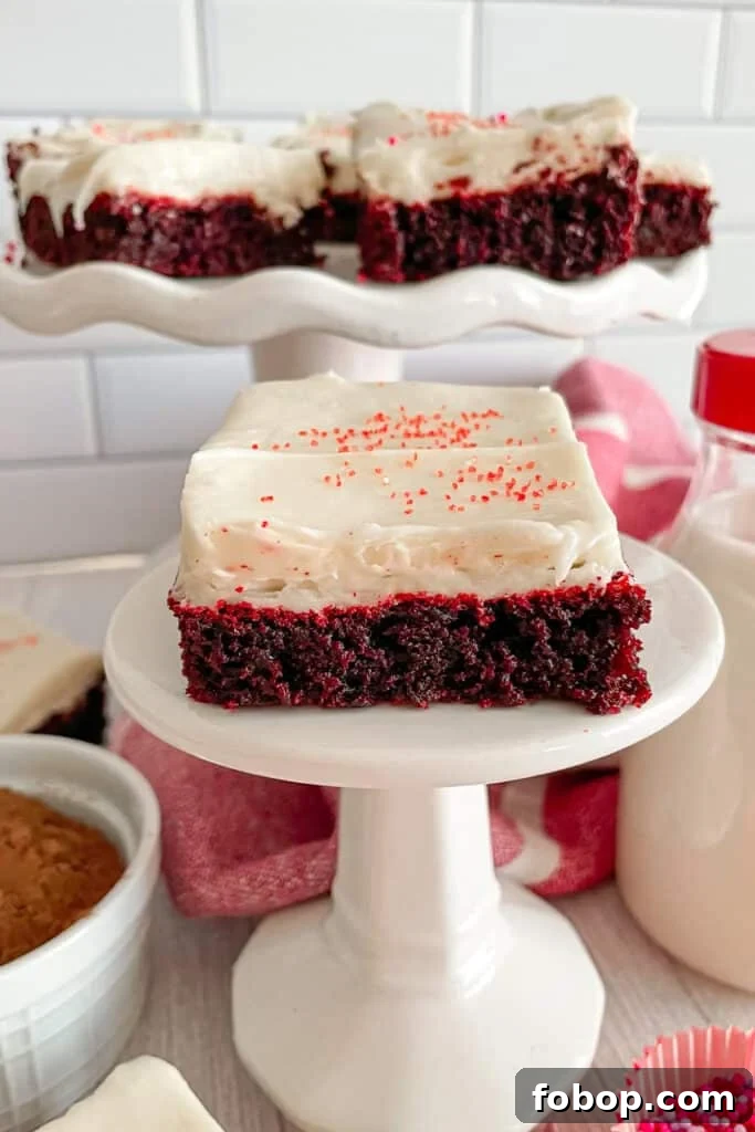 The best red velvet brownies with cream cheese frosting on a stand with brownies in the background
