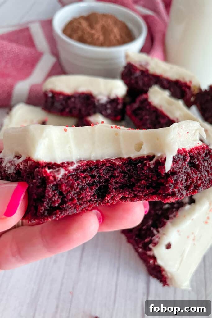 Close up shot of red velvet brownies with cream cheese frosting with a bite taken out of it and being held in a hand