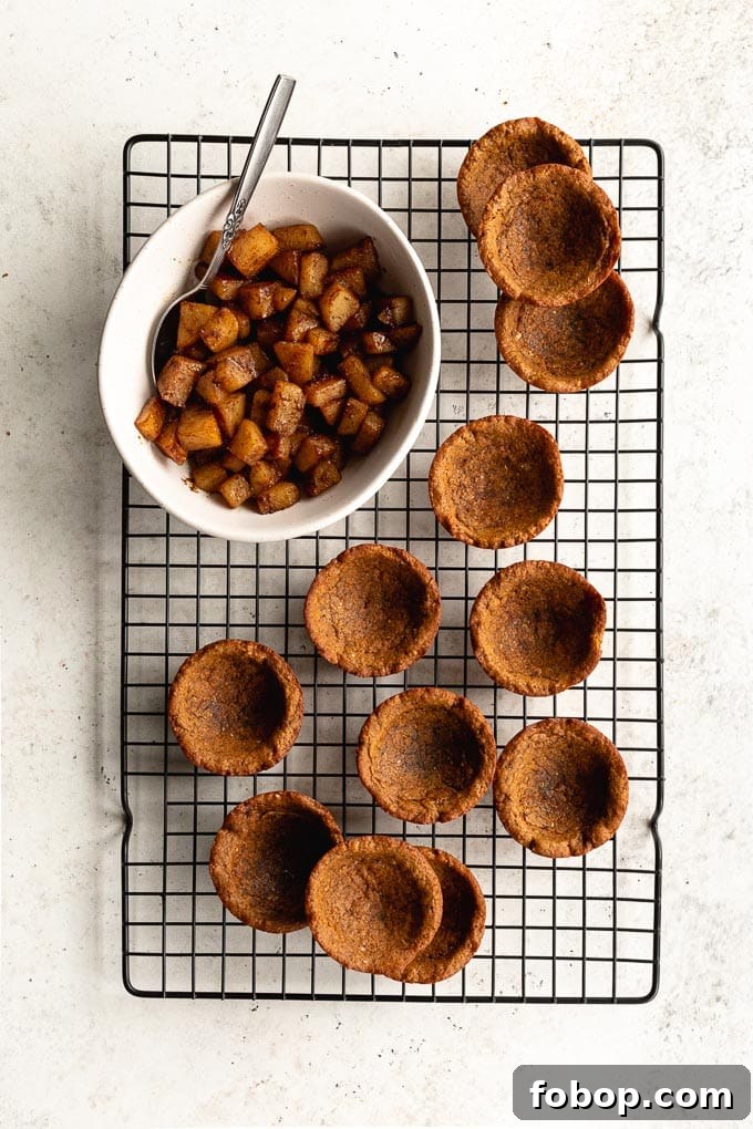 Cookie cups arranged on a black wire rack next to a bowl of sautéed pears.