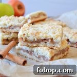two apple crumble bars stacked on parchment paper with cinnamon sticks
