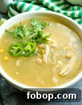 soup with cilantro and jalepeno peppers on top in a white bowl wit a green and white striped napkin