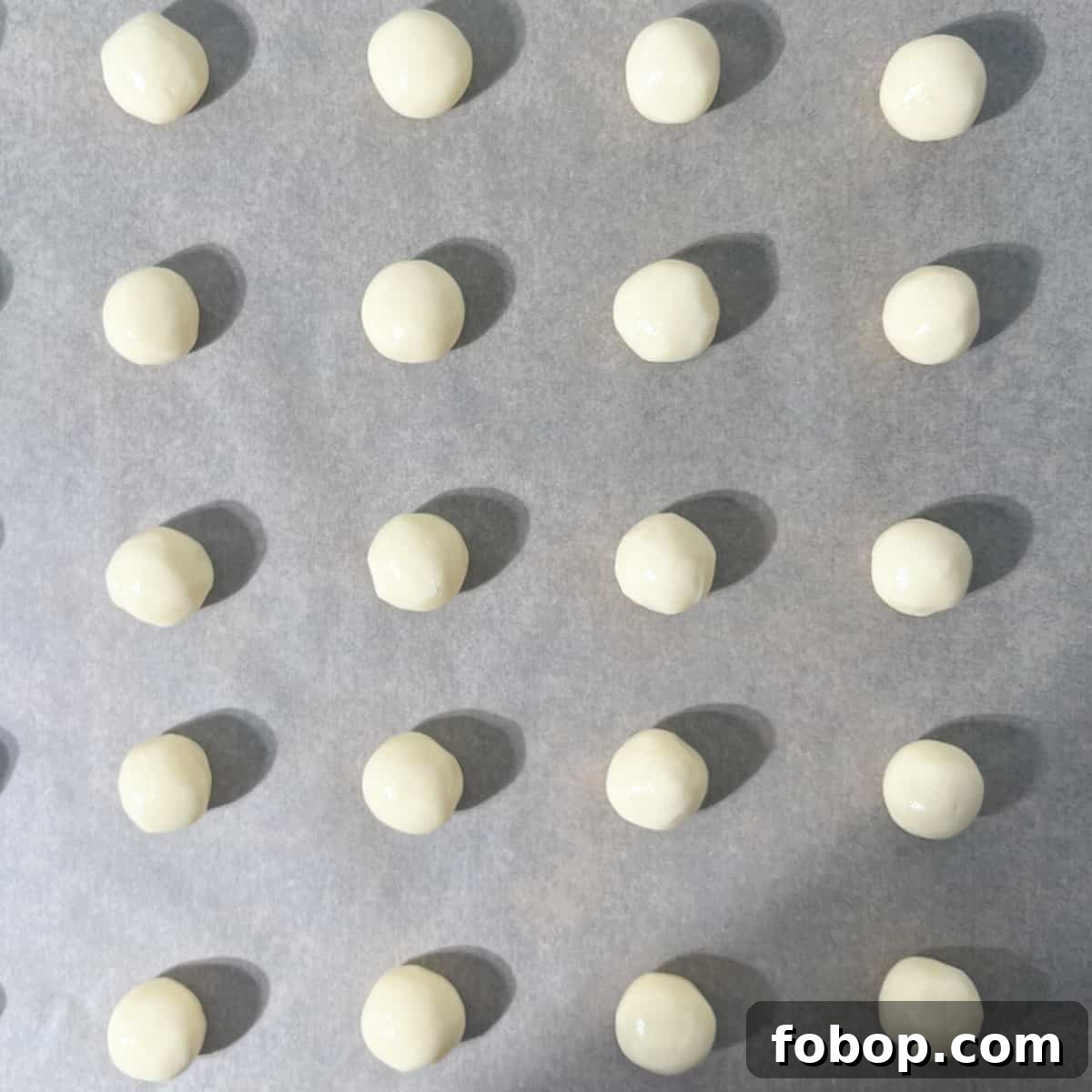 Dough balls on a large baking tray, ready to be flattened with a fork.