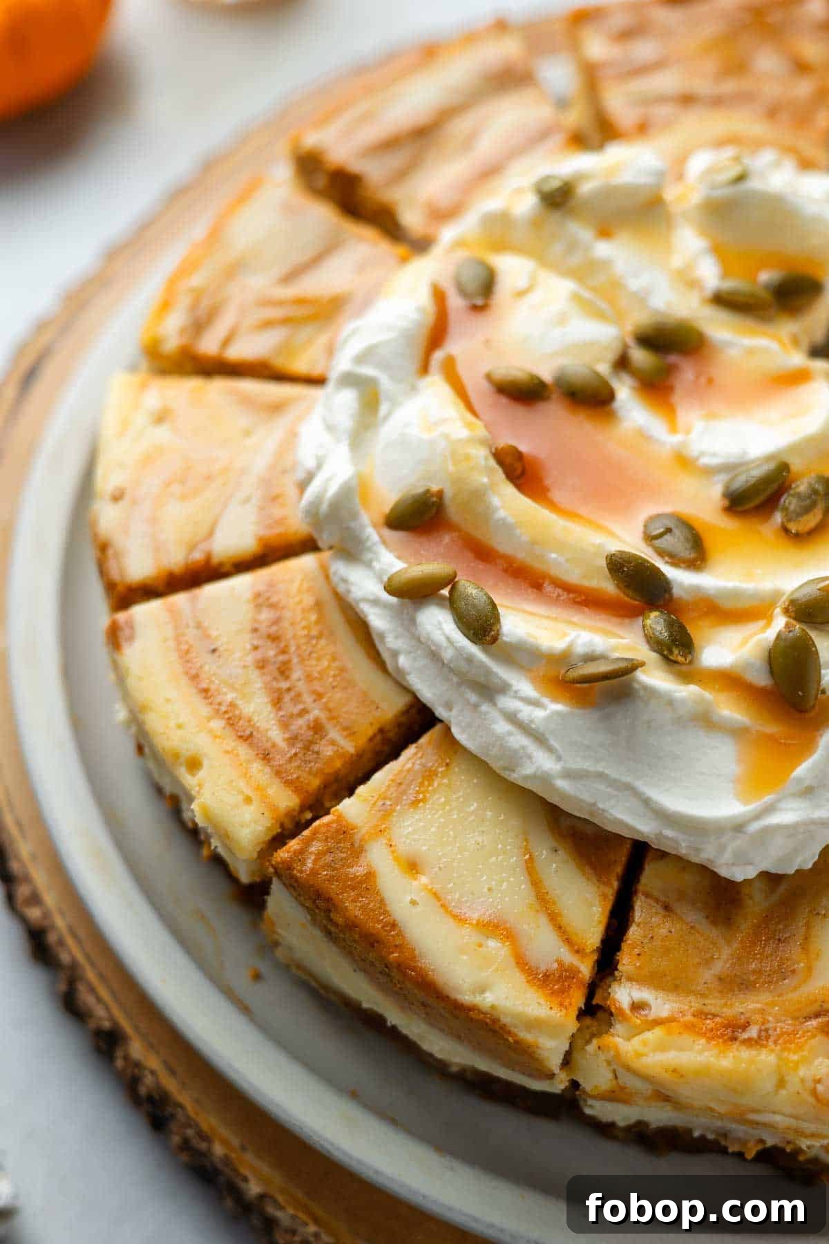 Gluten-Free Pumpkin Swirl Cheesecake sliced on serving plate topped with whipped cream, caramel sauce, and pepitas. 