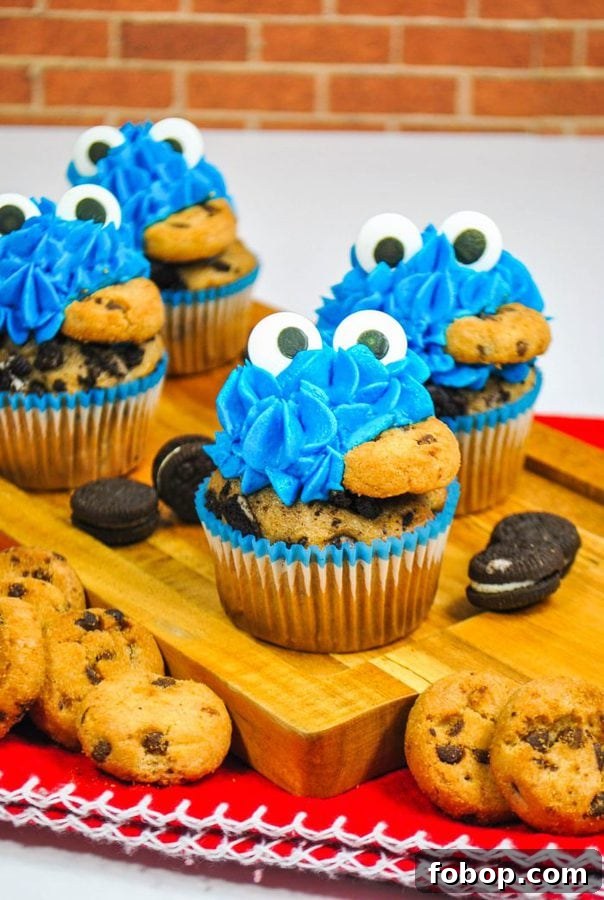Cookie Monster Cupcakes: Fun Blue Cookie Dough Cupcake Recipe 6 4 cookie monster cupcakes eating with candy eyes and a chocolate chip cookie in their mouths.