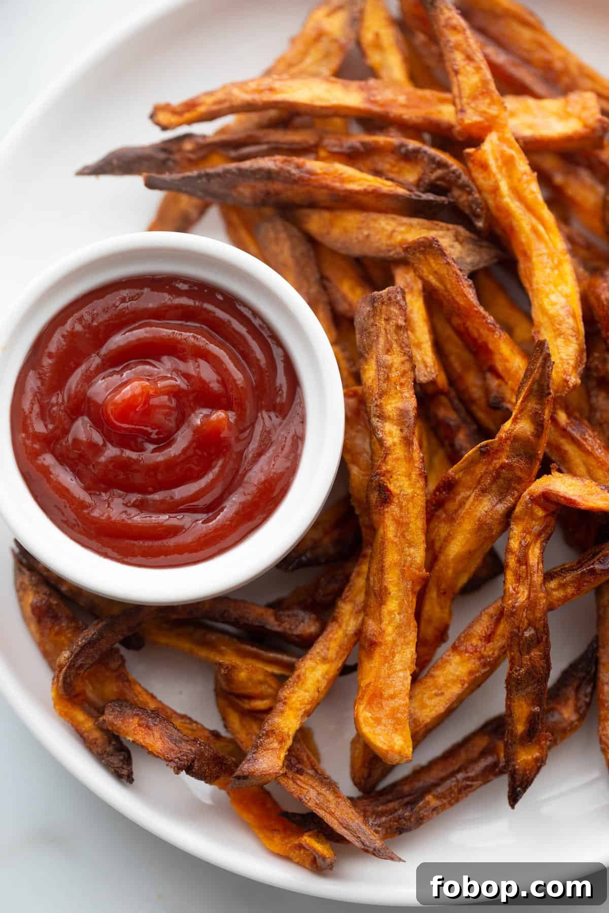 Crispy Air Fryer Sweet Potato Fries Recipe 3 Homemade sweet potato fries on a white plate with a side of ketchup.