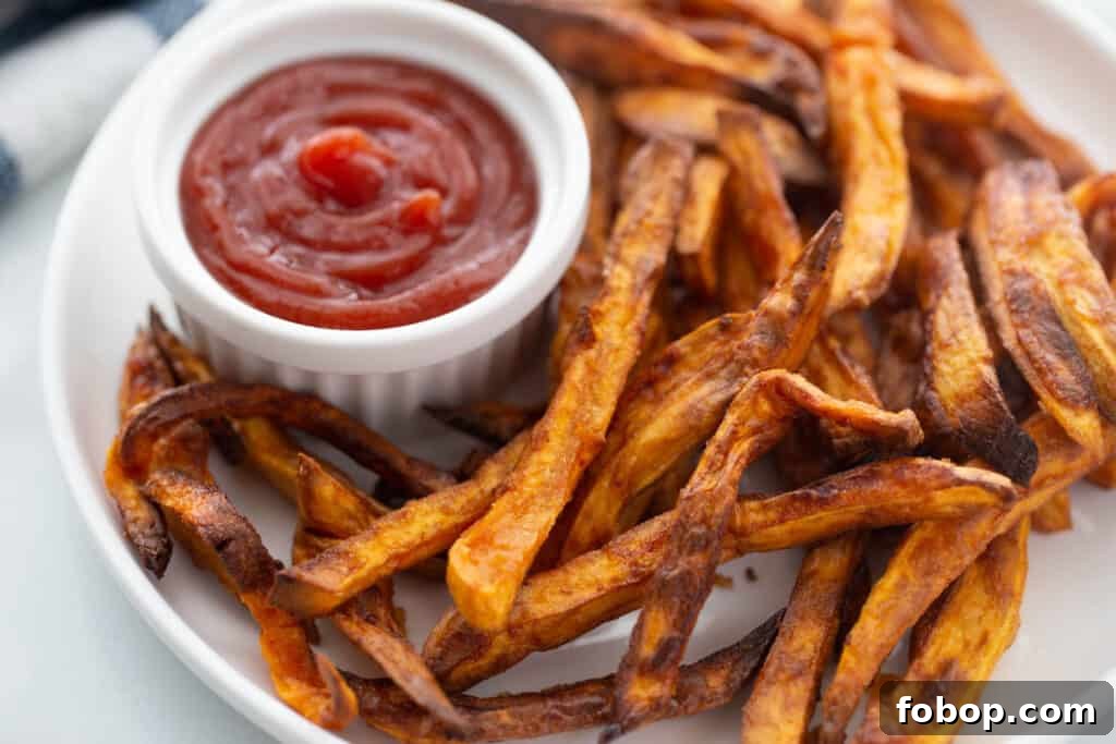 Crispy Air Fryer Sweet Potato Fries Recipe 10 Plate of crispy, golden brown air fryer sweet potato fries next to a ramekin of ketchup.