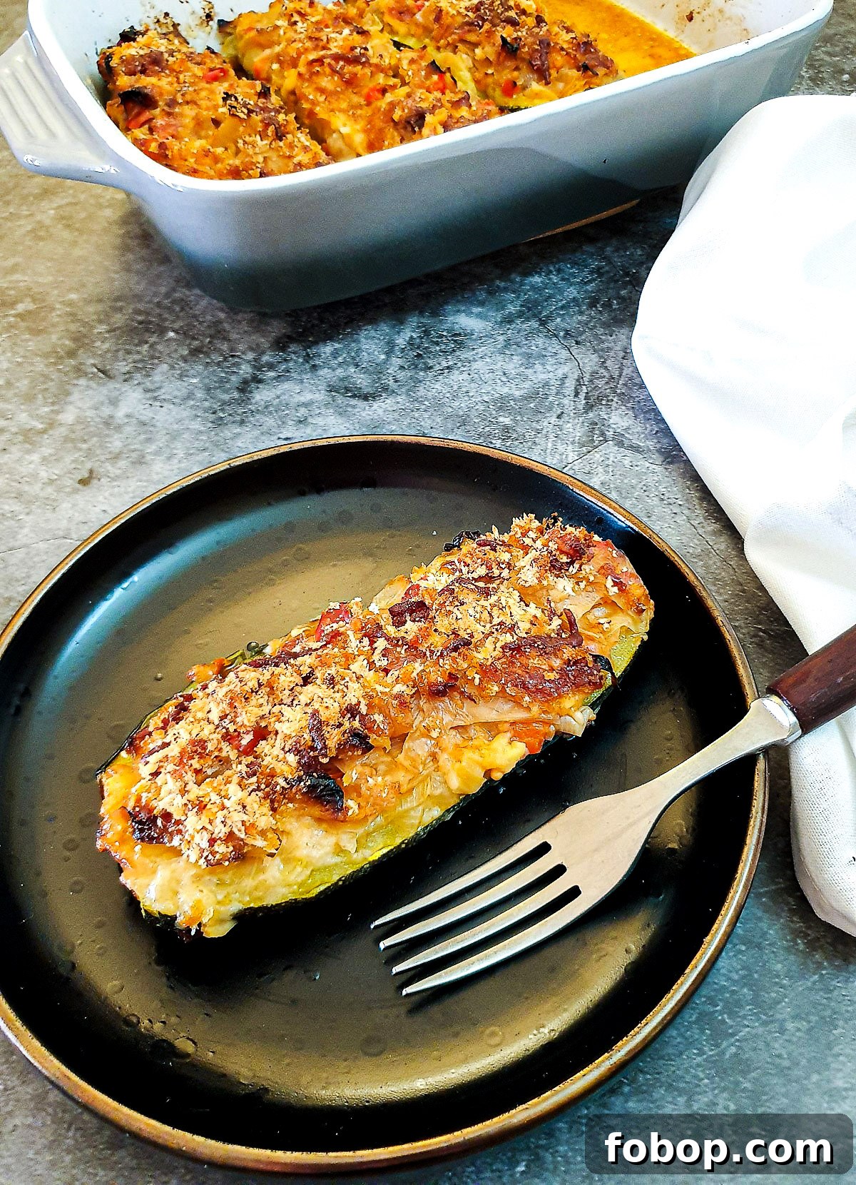 A cabbage-stuffed courgette with a cheesy topping on a brown plate with a fork.