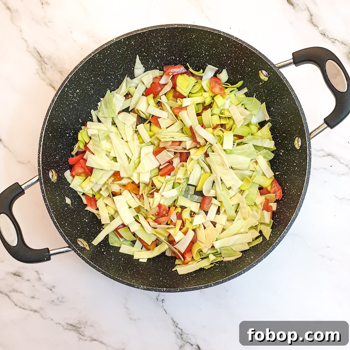 Shredded cabbage and leeks with tomatoes in a frying pan.
