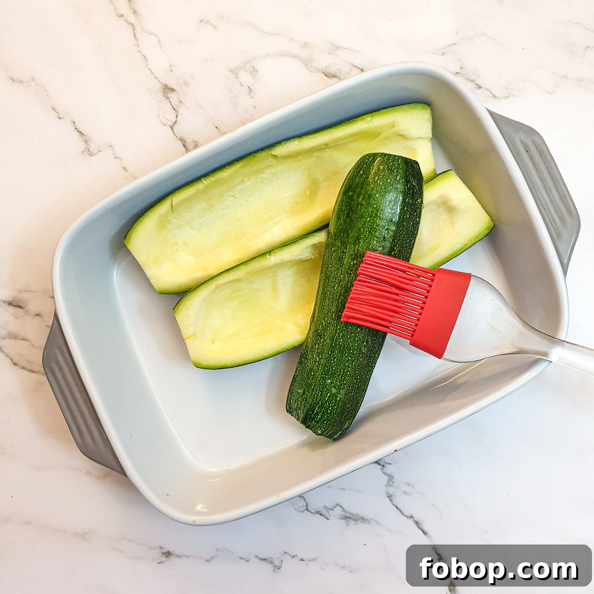 Hollowed out courgettes being brushed with oil.