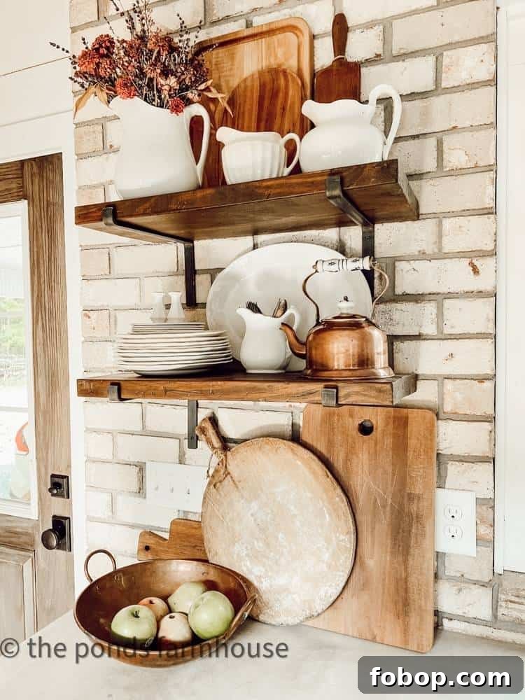 Open wood shelves on a white brick wall styled with ironstone, copper kettle, and wood cutting boards.