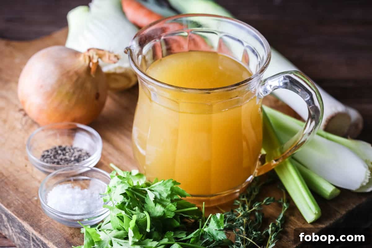 Homemade Chicken or Turkey Stock in a jug, a deep rich golden liquid, surrounded by vegetables and aromatics.