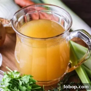 Homemade Chicken or Turkey Stock in a jug, a deep rich golden liquid, surrounded by vegetables and aromatics.