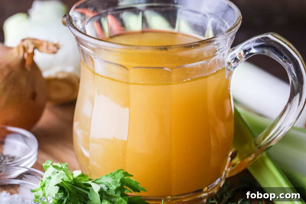 Homemade Chicken or Turkey Stock in a jug, a deep rich golden liquid, surrounded by vegetables and aromatics.