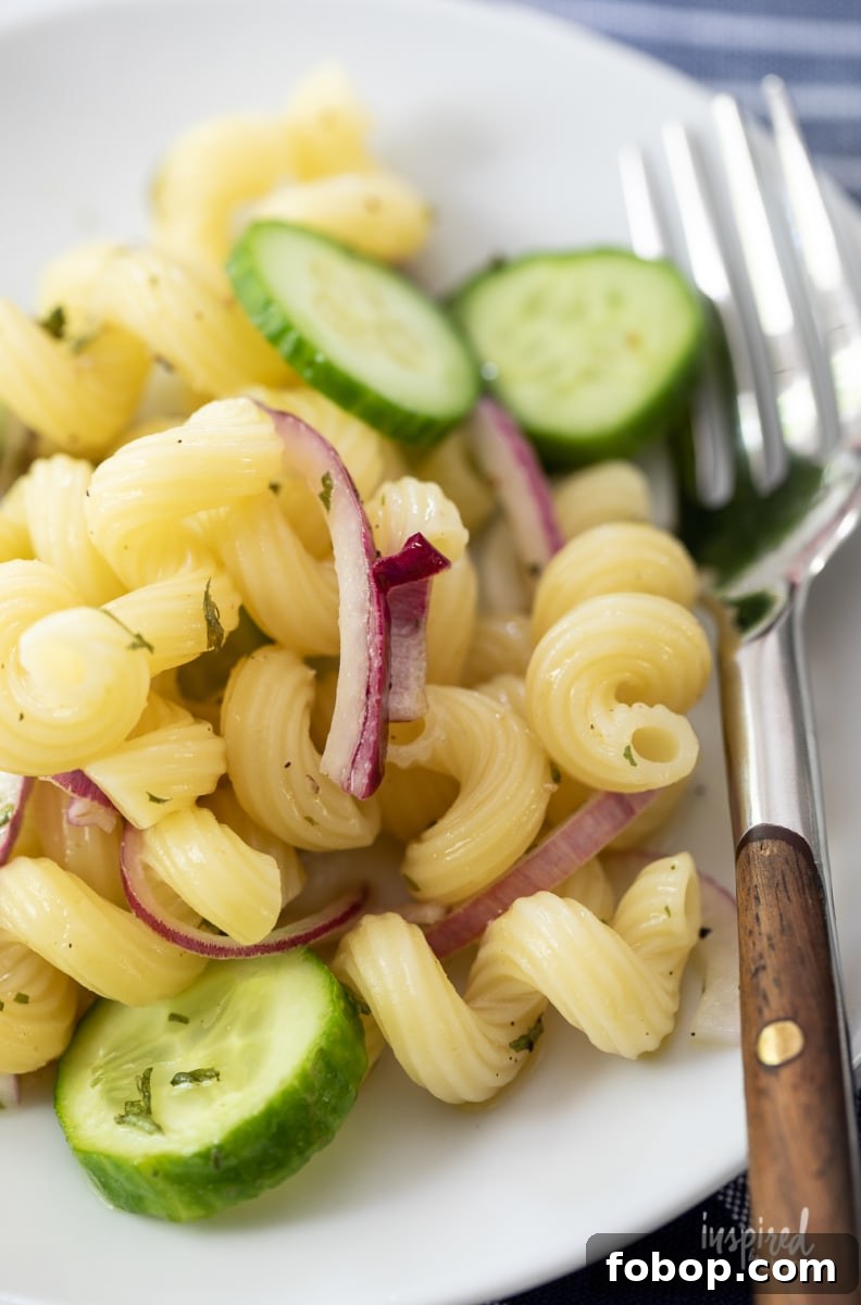 close up of cucumber pasta salad with red onions on a plate with a fork.