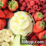 bananas, strawberries, raspberries and green apples surrounding yellow lemon fruit dip in the center