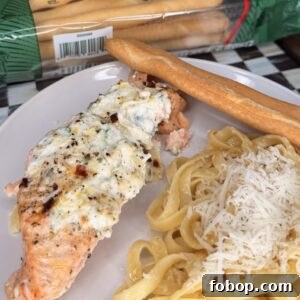 Lemon Ricotta-Stuffed Salmon with Herbed Citrus Sauce 11 A plate with baked salmon topped with creamy cheese and herbs, fettuccine pasta sprinkled with grated cheese, and a breadstick. In the background, a package of Italian breadsticks is visible.