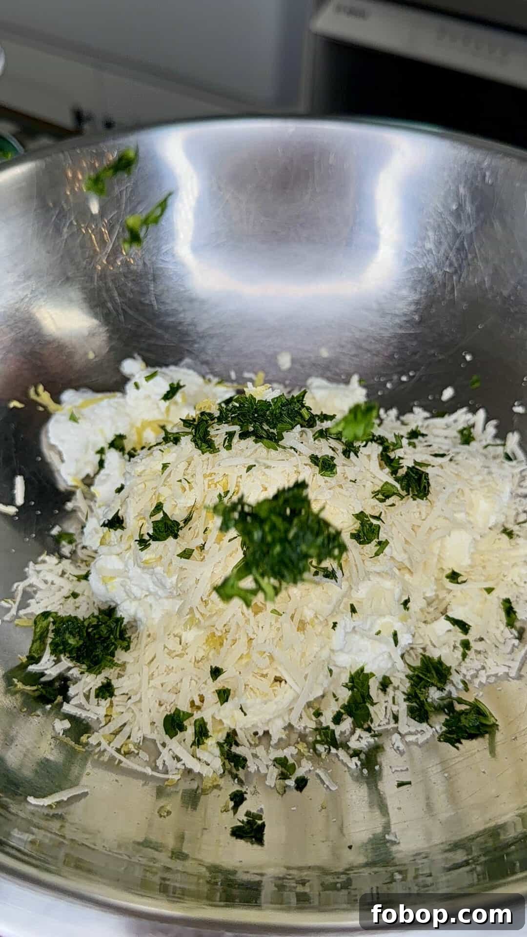 Lemon Ricotta-Stuffed Salmon with Herbed Citrus Sauce 3 A stainless steel mixing bowl containing shredded cheese, ricotta cheese, and chopped fresh herbs, ready to be mixed together.