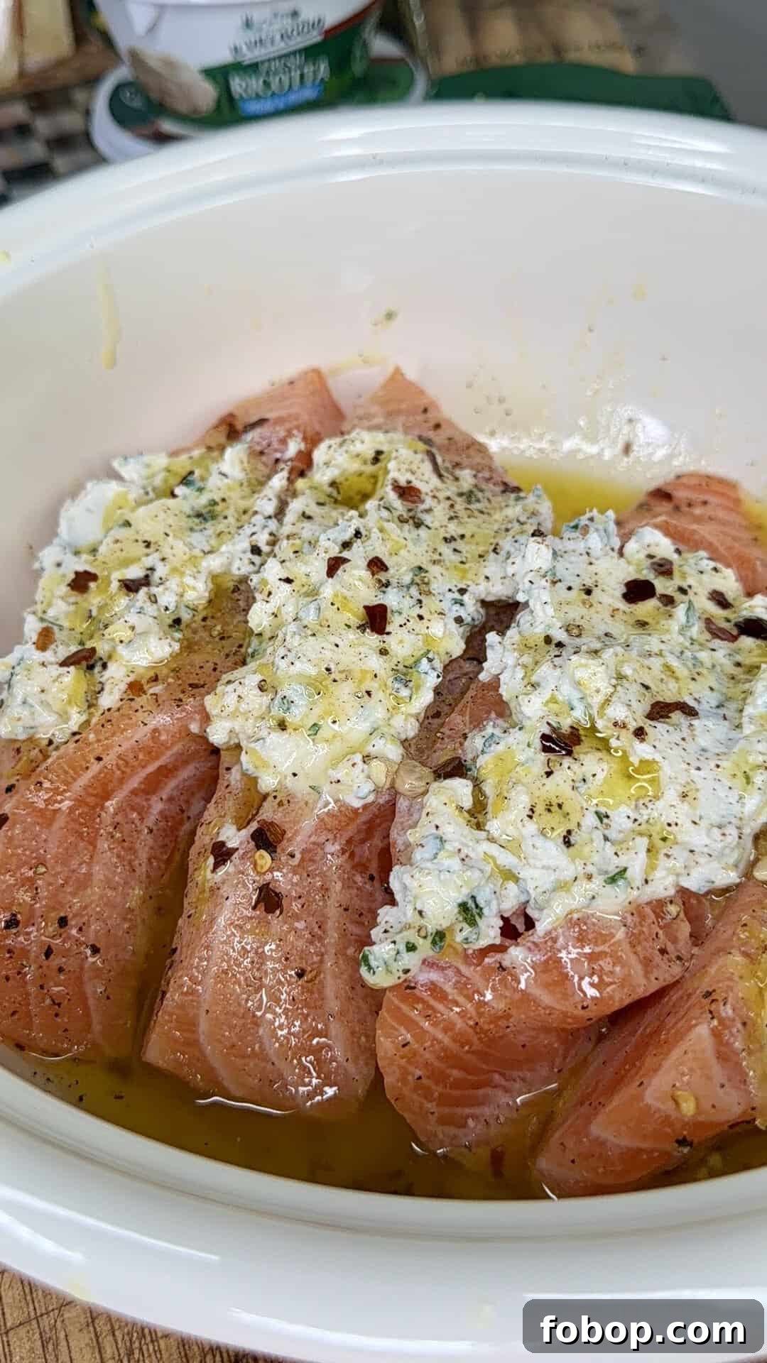 Lemon Ricotta-Stuffed Salmon with Herbed Citrus Sauce 8 Raw salmon fillets in a white dish topped with a creamy herb mixture, black pepper, red pepper flakes, and drizzled with olive oil, ready to be cooked.