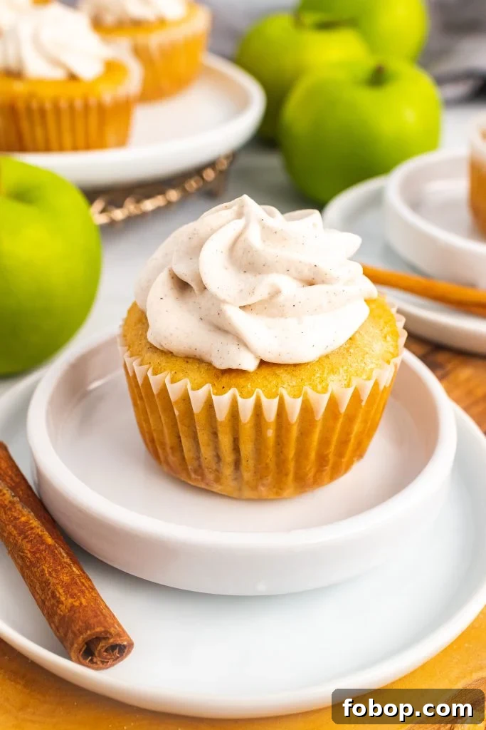 filled apple pie cupcake topped with cinnamon whipped cream & sitting on a small white plate