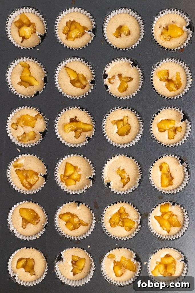 batter for apple pie cupcakes prepared in muffin tin with dollops of pie filling in the center